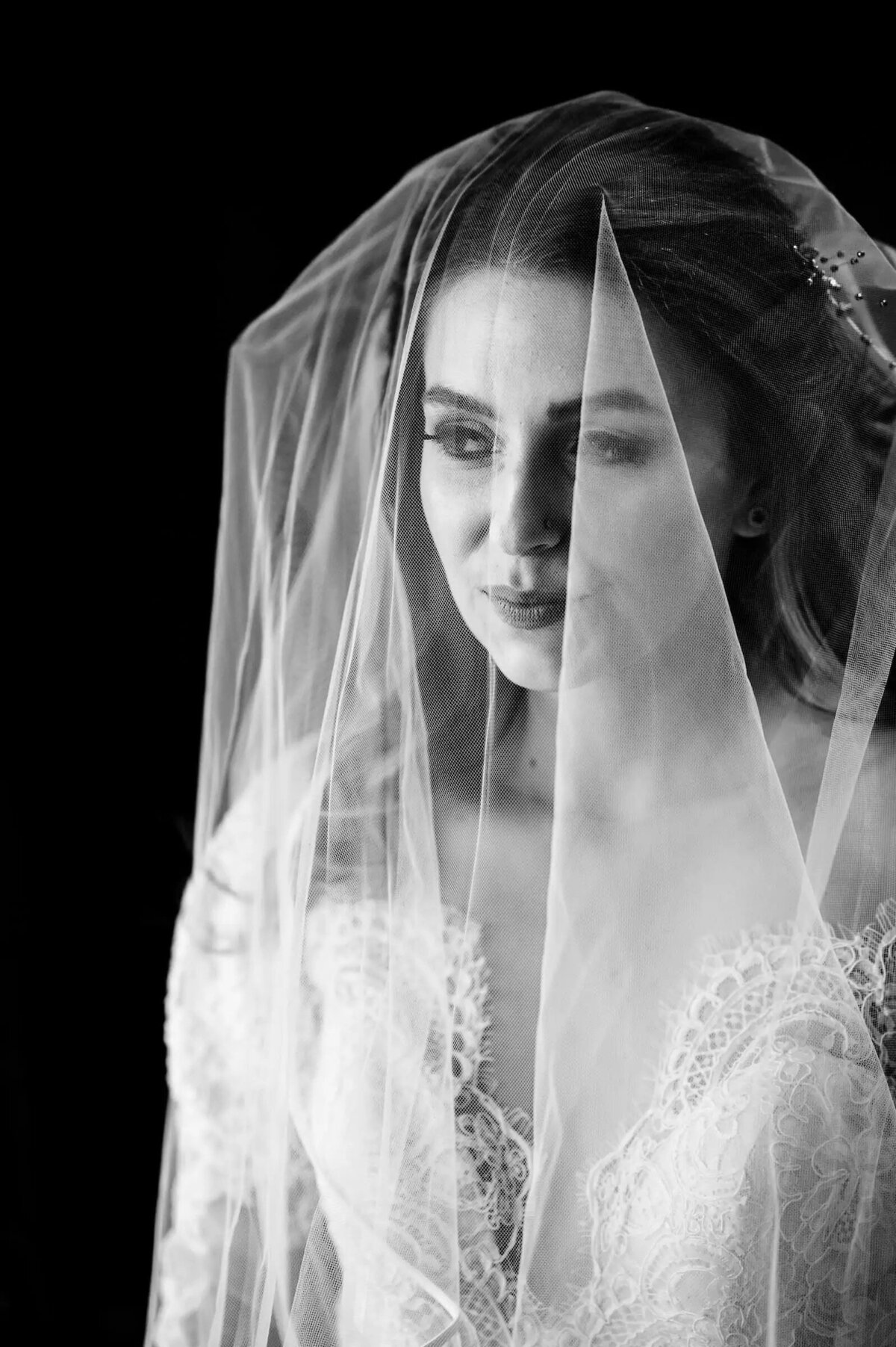 A soft and ethereal portrait of a bride looking downward, her face partially veiled, creating a sense of introspection and bridal elegance.