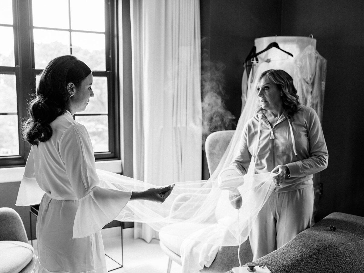 Black and white photo of bride and mom steaming wedding dress and veil before wedding in Georgetown DC