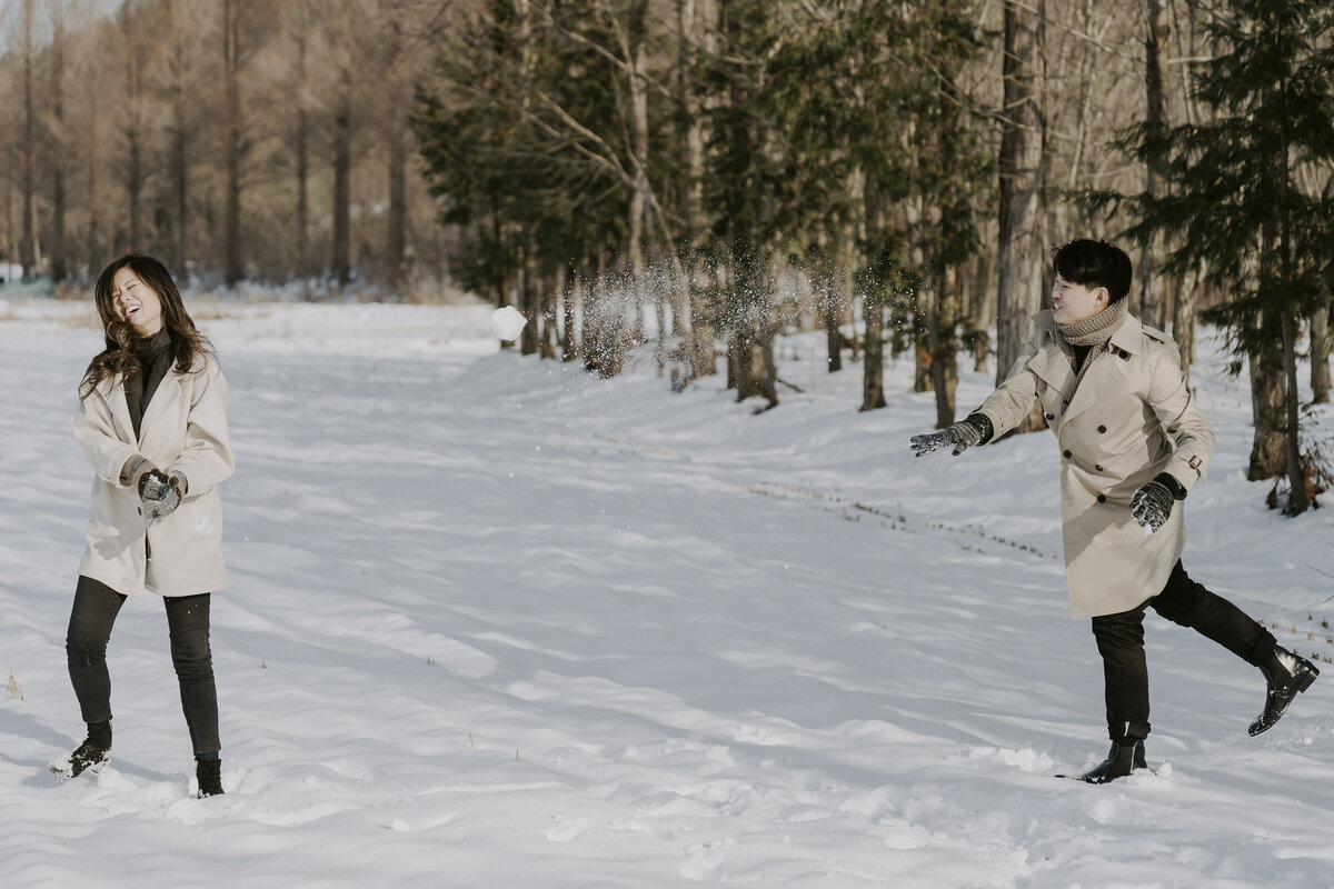 the groom throws back snow ball to the bride and she is laughing