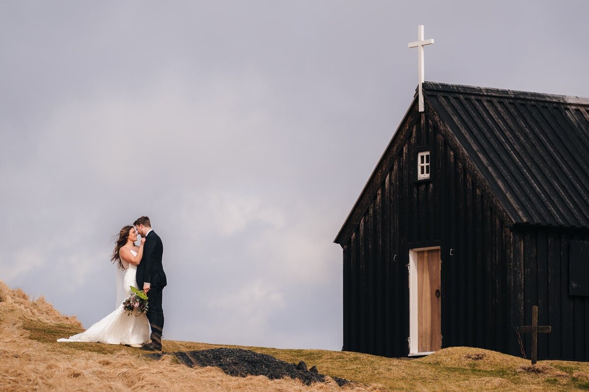 This couple shares a sweet kiss in front of a quaint Icelandic church, sealing their love amidst the charm of the surroundings.