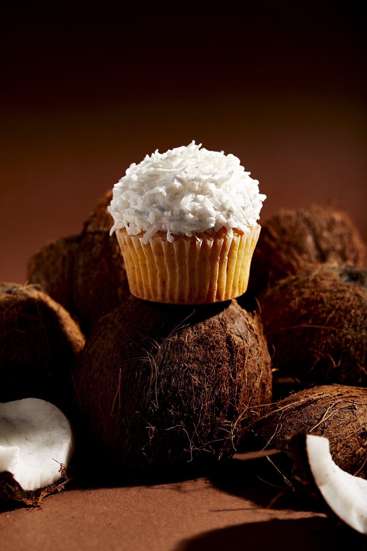 A coconut cupcake on top of a full coconut.