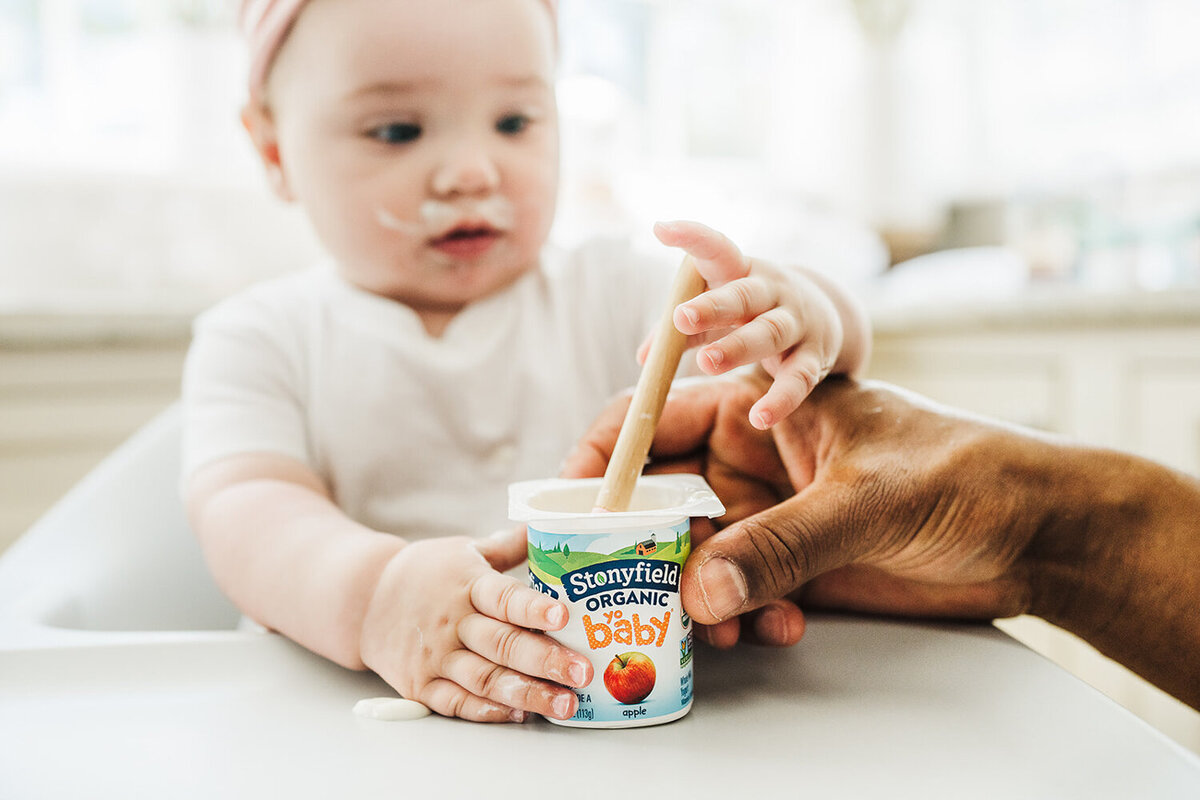baby reaches for spoon in yogurt cup for commercial branding images
