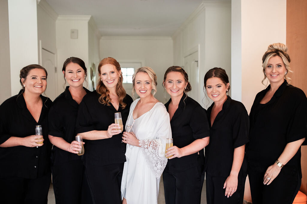 Bride in white robe with bridesmaids in black robes
