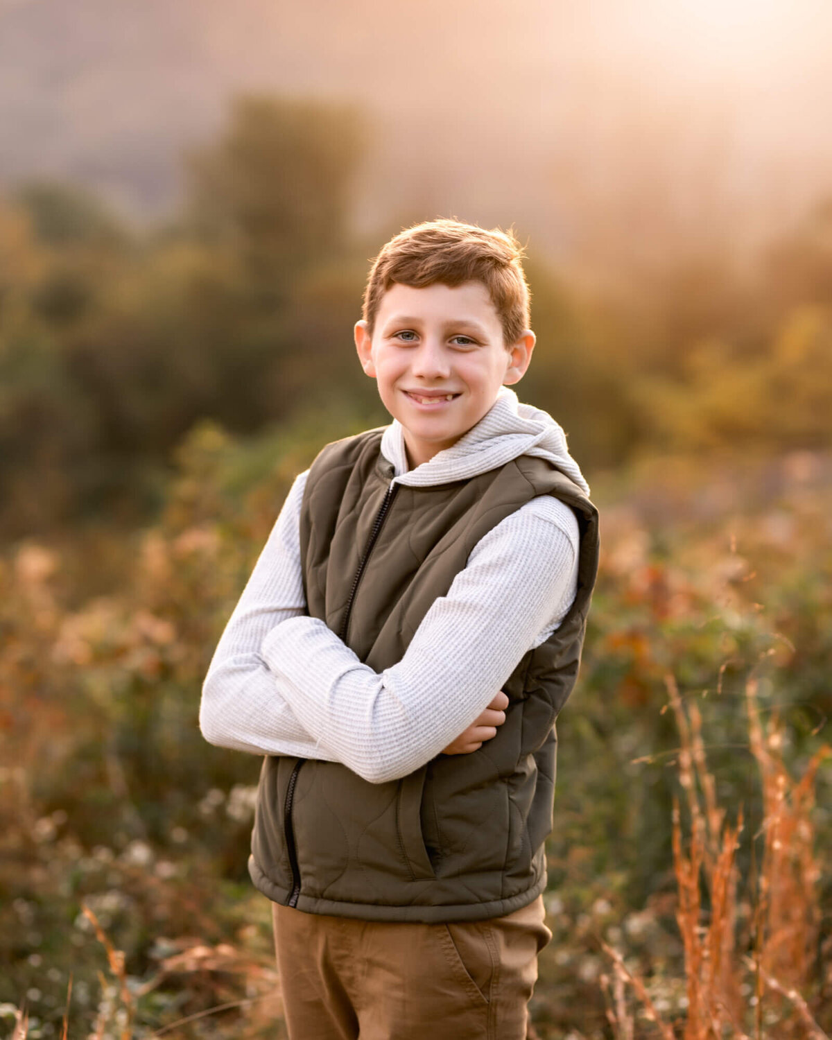 A tween boy in a green vest posing the tall grass during a portrait session with an Asheville Family Photographer