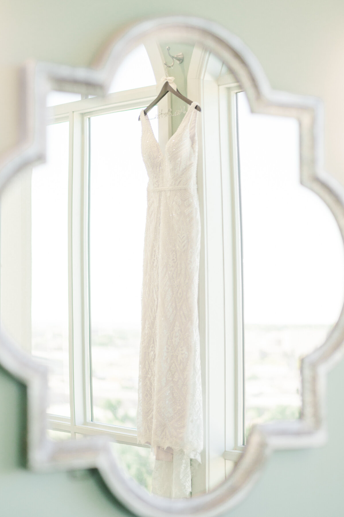 A white wedding dress hanging in the window photographed through a mirror at the Pinery at the Hill.