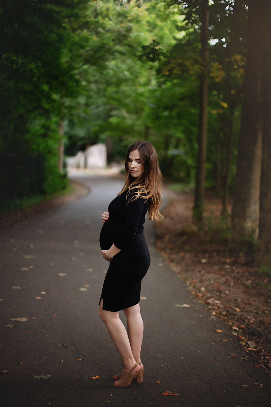 pregnancy pictures mom holding belly black dress on park path
