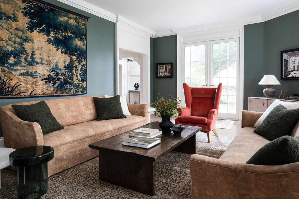 Bold living room with beige couches, green velvet ottoman and patterned artwork