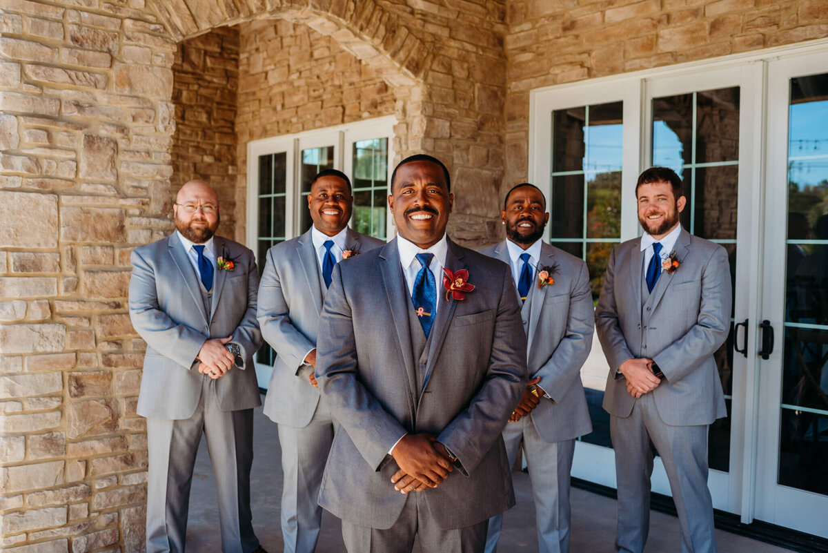 photo of a groom standing and smiling while his groomsmen are smiling behind him