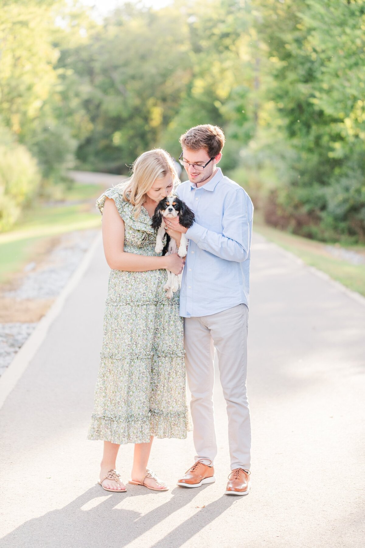 Wife kisses her cute dog while husband smiles at them on the Murfreesboro Greenway during spring