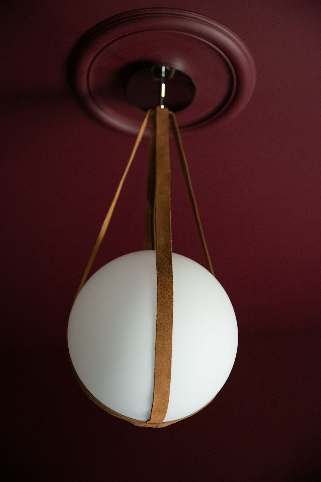 a chandelier made of a white ball with brown leather straps