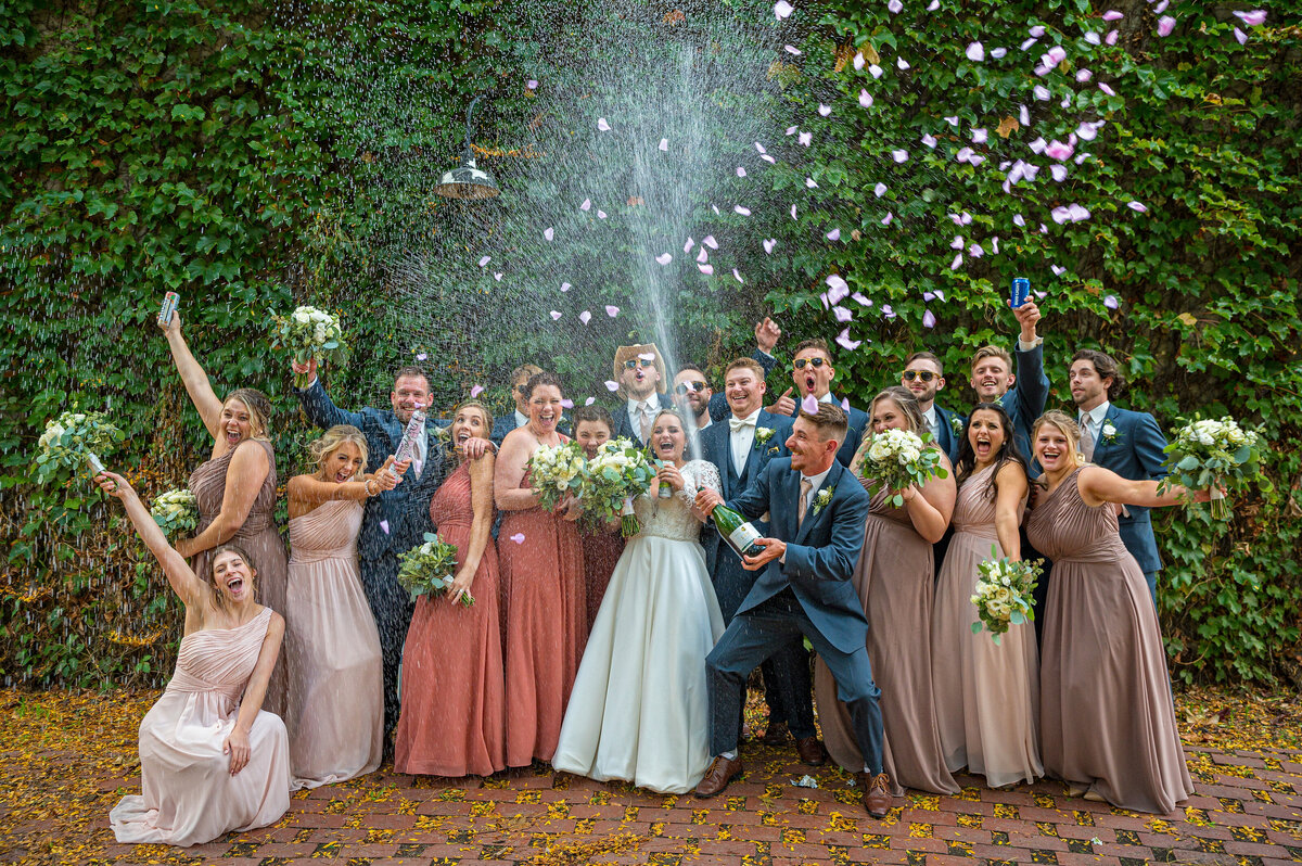 Wedding group partying popping champagne and throwing rose petals.