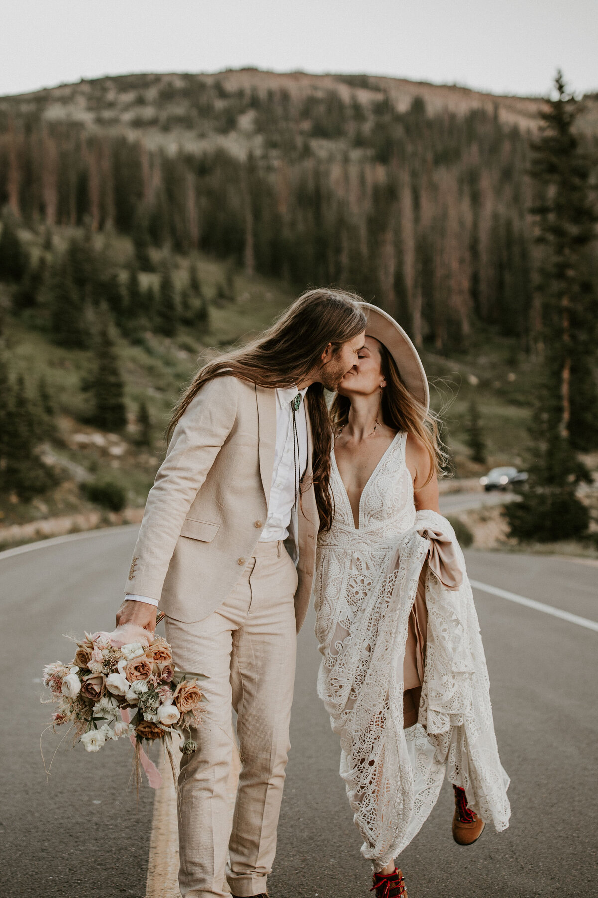 Bride and groom wearing an ivory dress and suit kissing in the middle of the road with mountains in the background