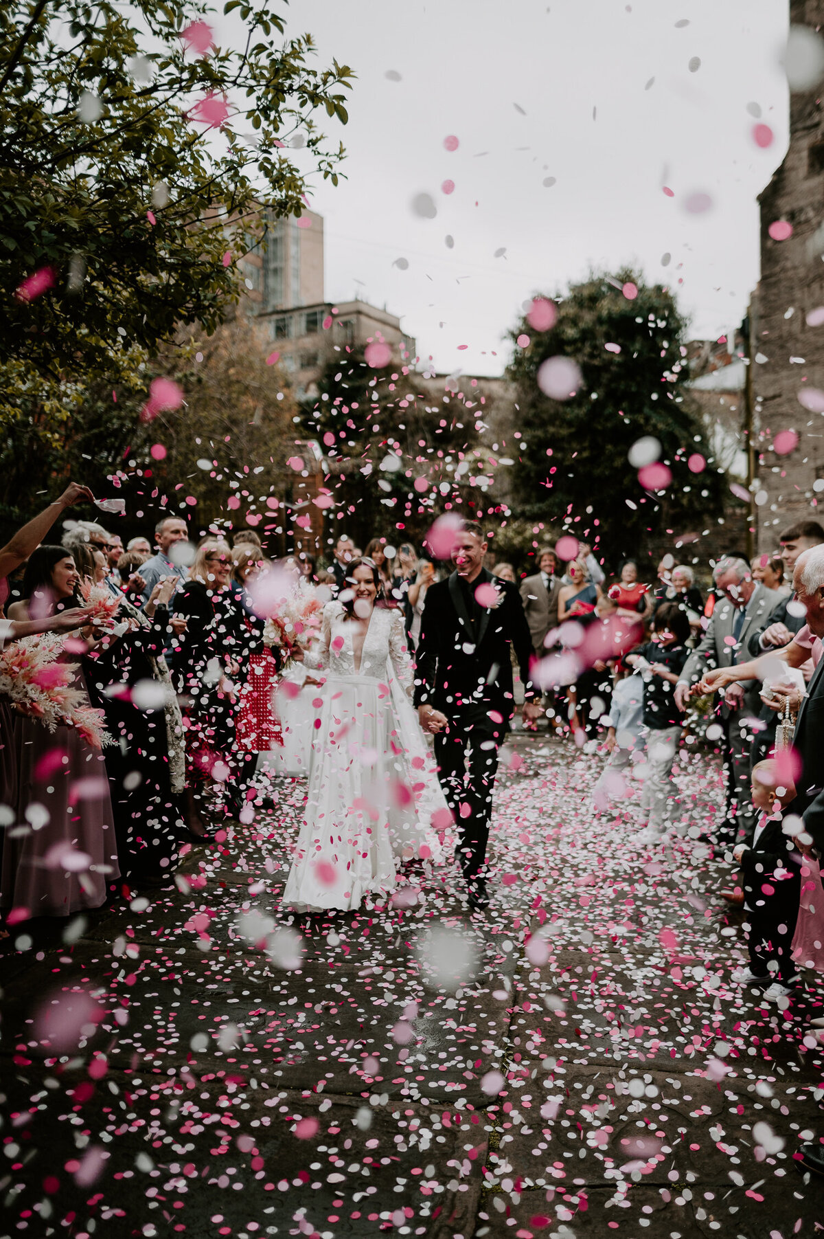 Guests throw pink confetti as a bride and groom exit The Mount Without in Bristol.