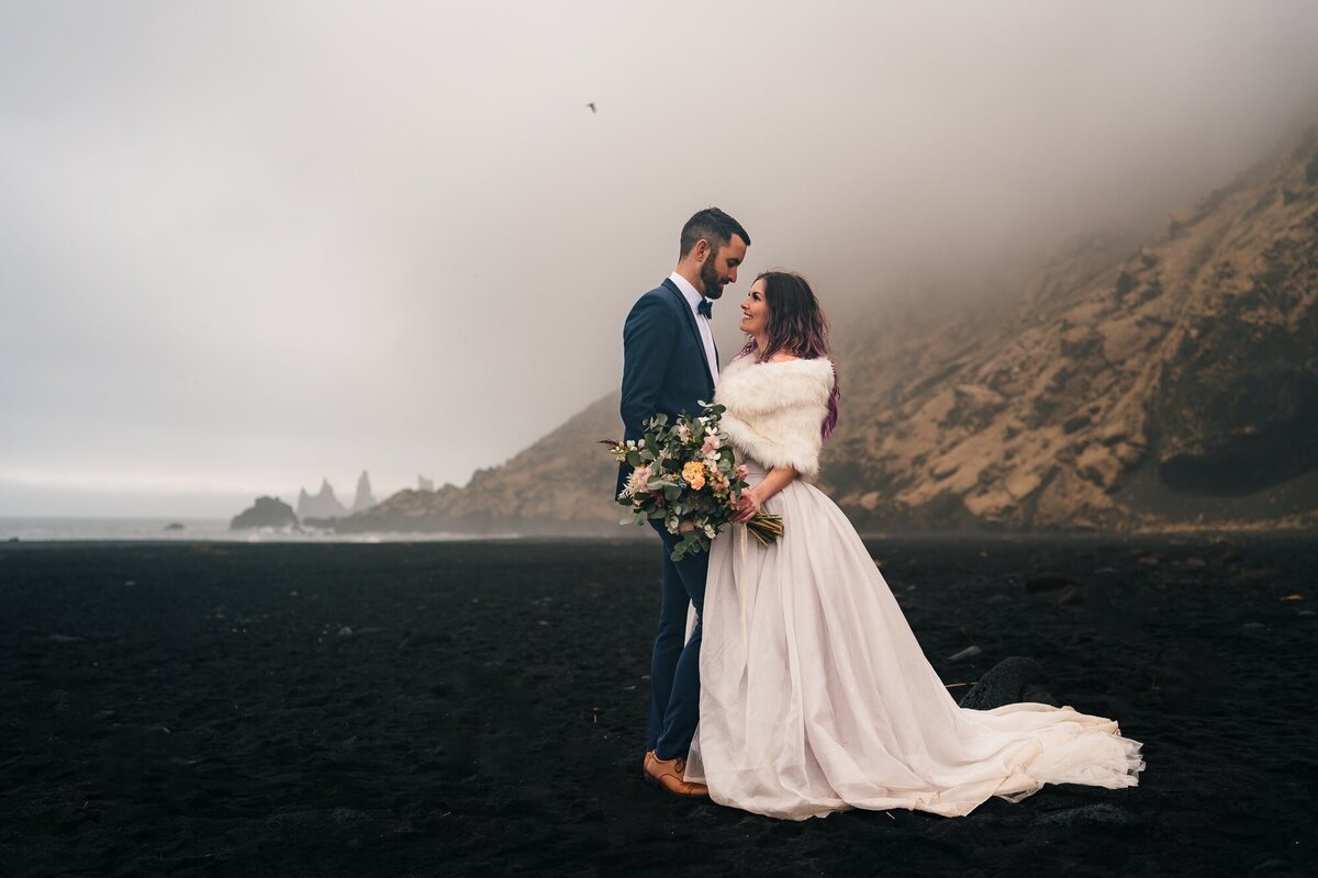 On the black sands of an Icelandic beach, this couple shares a moment, looking into each other's eyes and finding the beauty of their connection in the stunning surroundings.