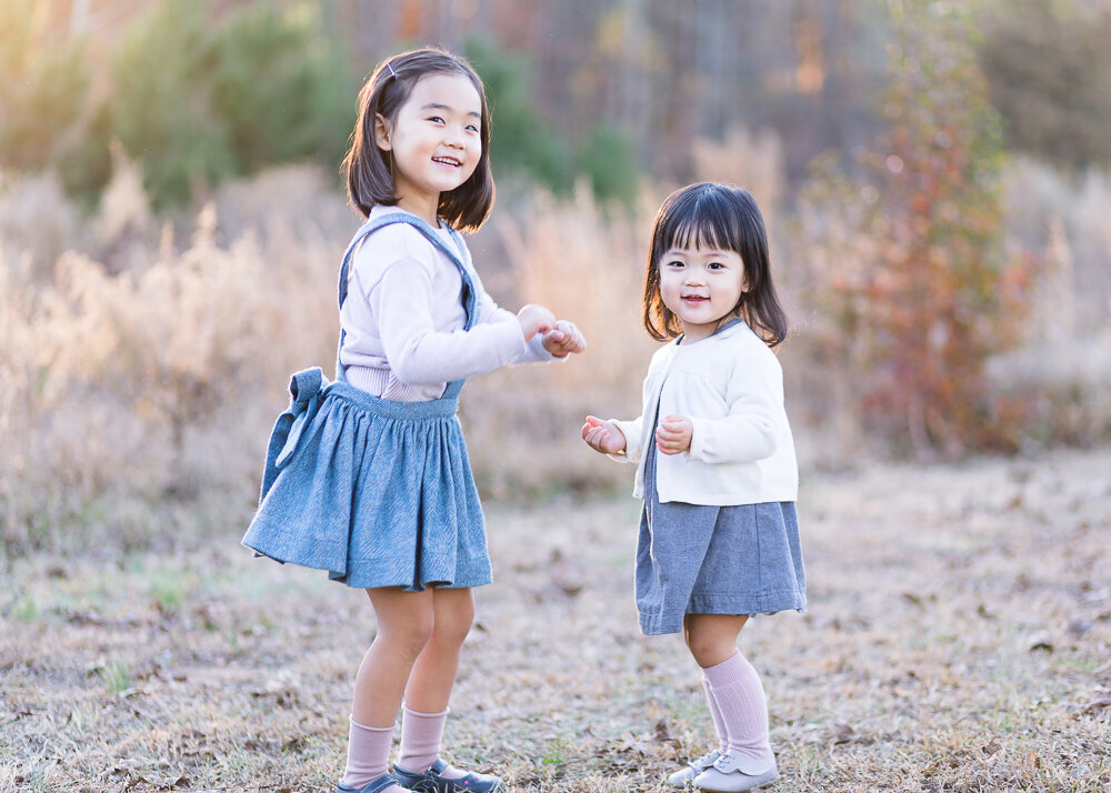 Outdoor family photo session with two little sisters dancing at a field.