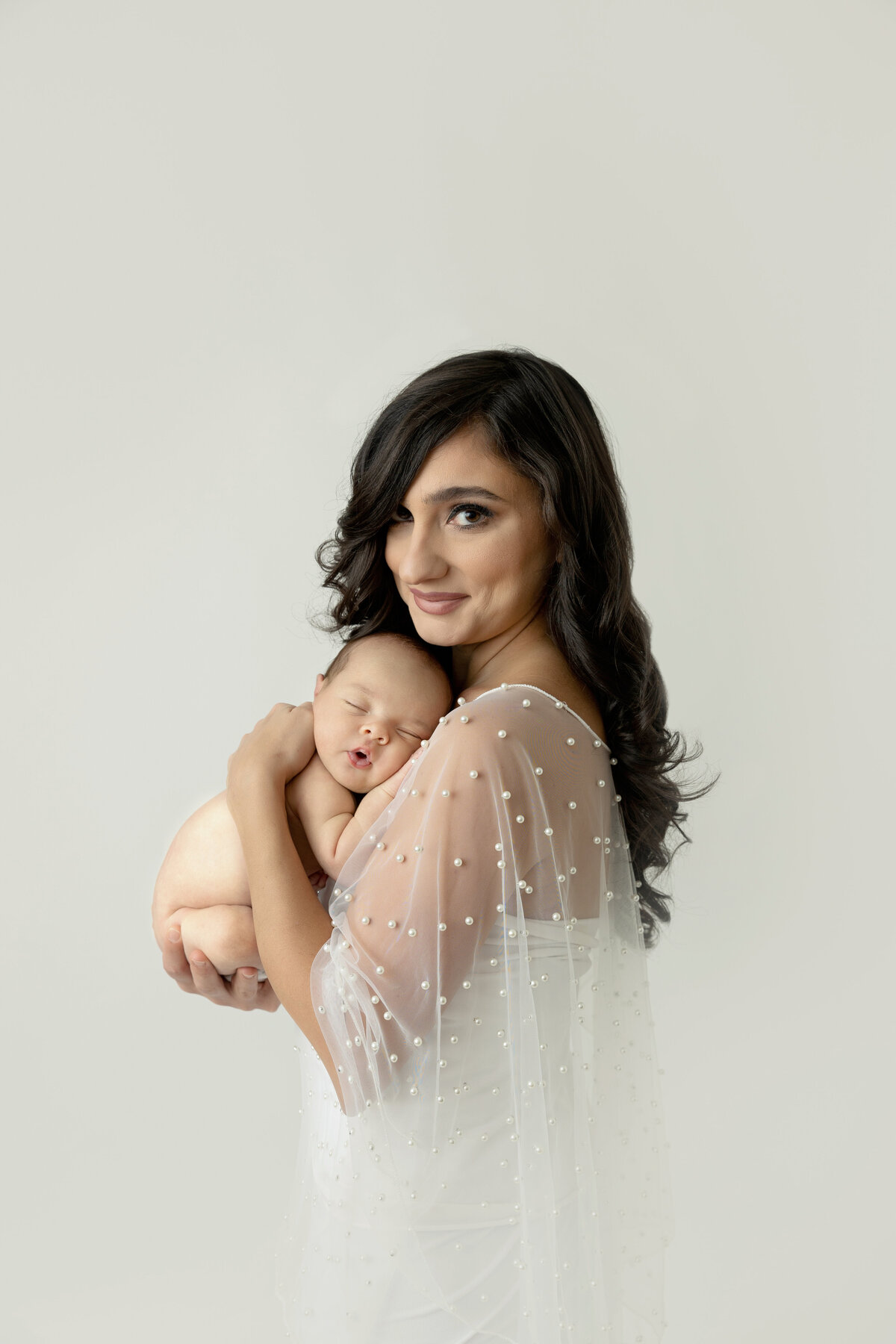 A happy mother in a whtie dress cradles her sleeping newborn against her chest