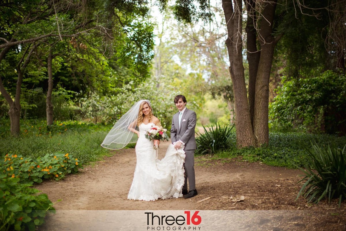 Newly married couple pose in the Fullerton Arboretum woods as the Groom carries his wife's dress train