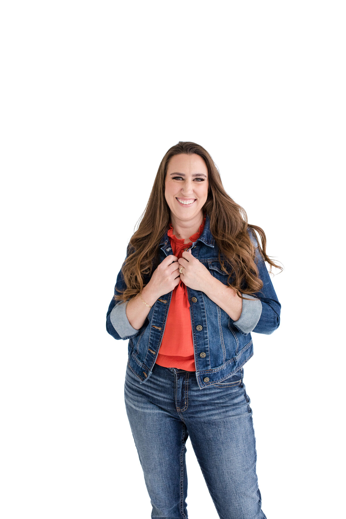 brand photographer near me captures brand photo of woman in a red blouse and denim jacket on a white background holding her jacket and smiling