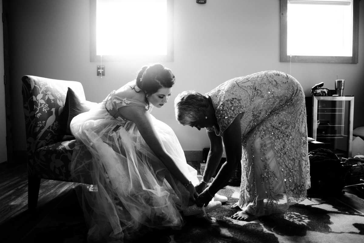 One of the top wedding photos of 2020. Taken by Adore Wedding Photography- Toledo, Ohio Wedding Photographers. This photo is of a mother helping the bride put her shoes on before the wedding ceremony