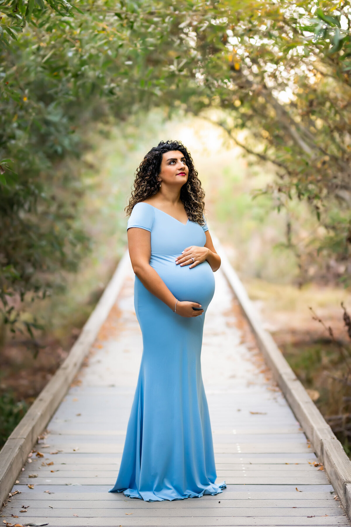 Portrait of pregnant woman holding her belly and looking up while standing on the bridge walkway at San Elijo Lagoon and Nature Center