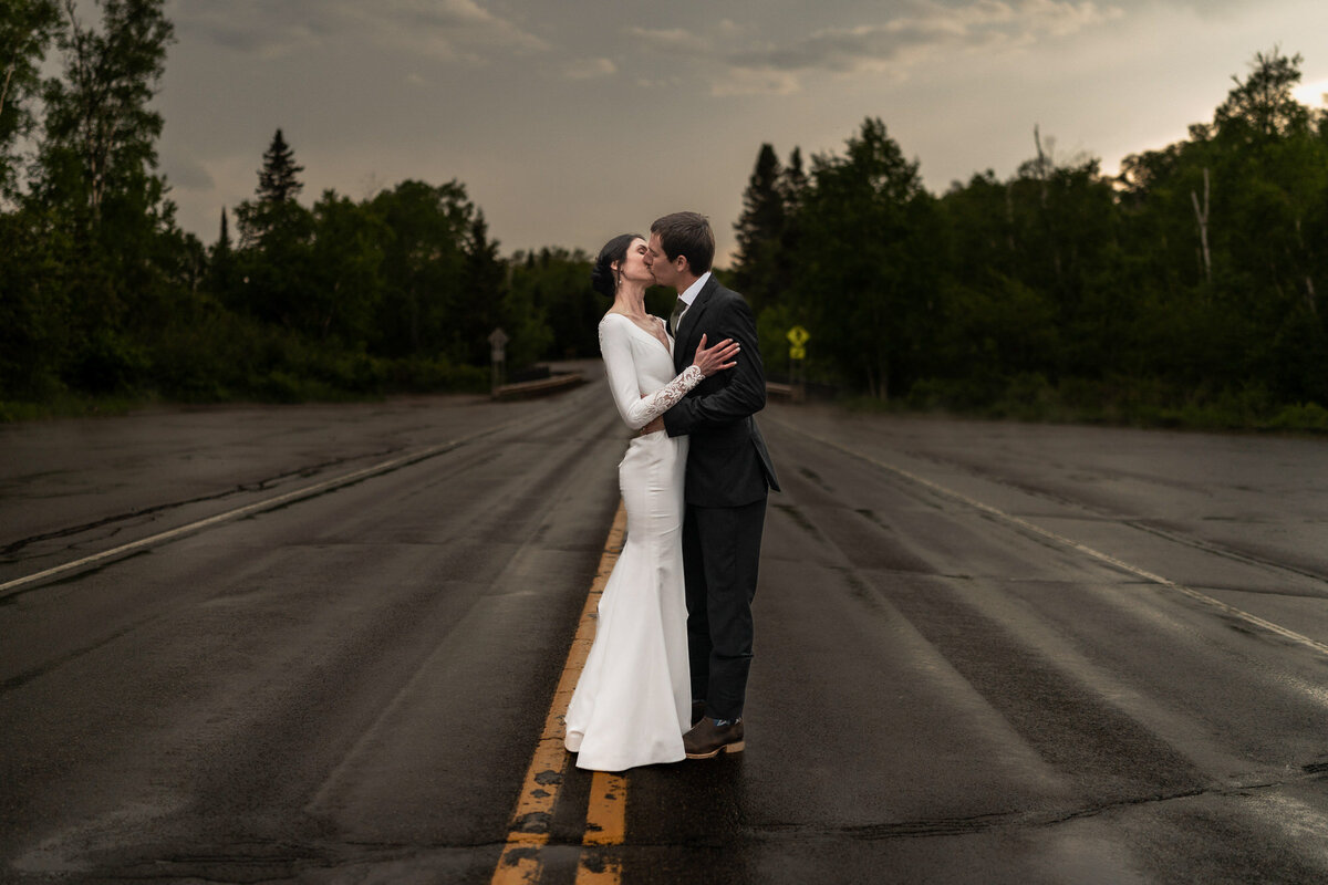 Bride and groom kiss in the middle of the road on a rainy day.