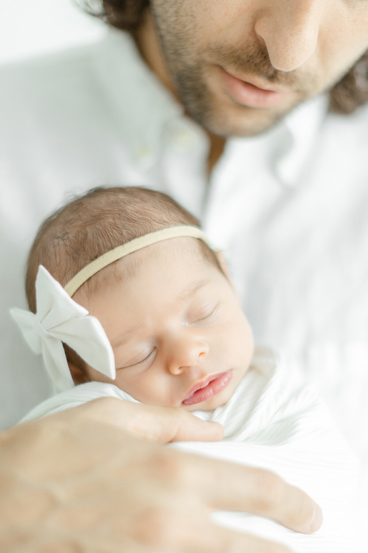 Close up photo of a beautiful newborn baby girl as her father holds her for their in studio newborn session.