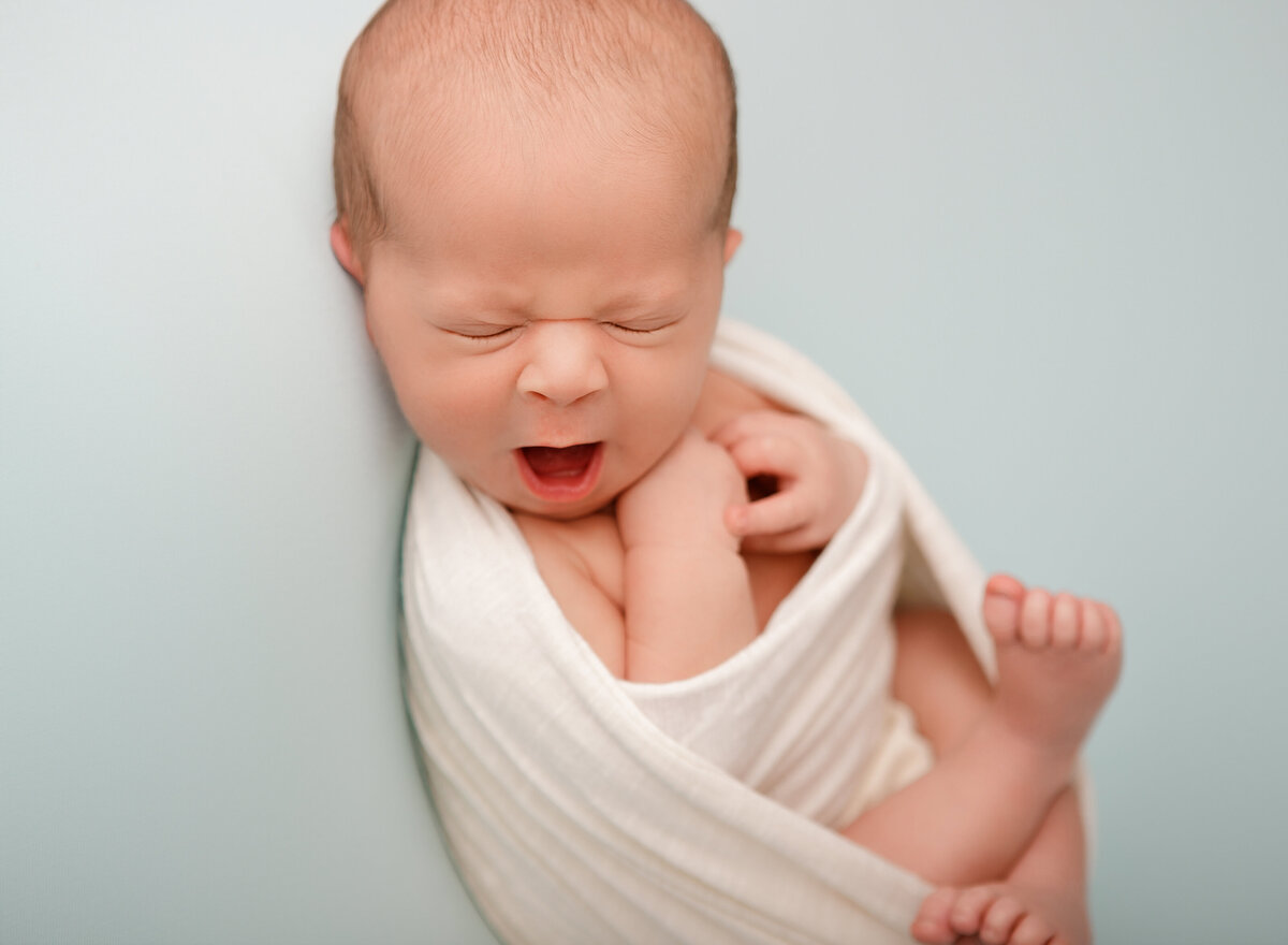 Yawning newborn shot on a mint backdrop