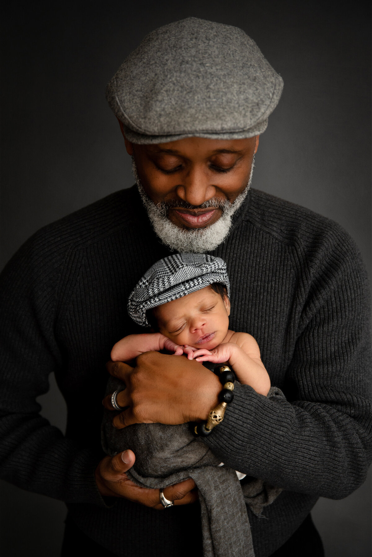 st-louis-newborn-photographer-father-with-beard-holding-newborn-baby-wearing-matching-flatcap-hats-in-gray-varient-color-scheme