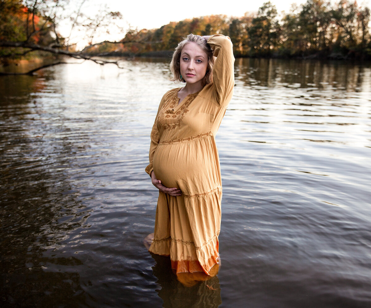 A young mother holds her baby bump in the river at Marinet Point Park during her maternity photoshoot.