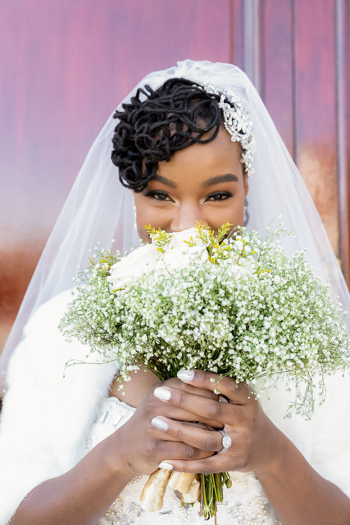 A young Black bride is smelling her baby breathe( green and white) flowers near a wooden door at The Merion Catering.