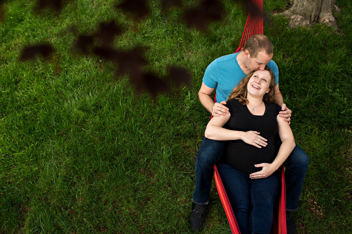A pregnant couple lay in their hammock in the back yard during home maternity session.