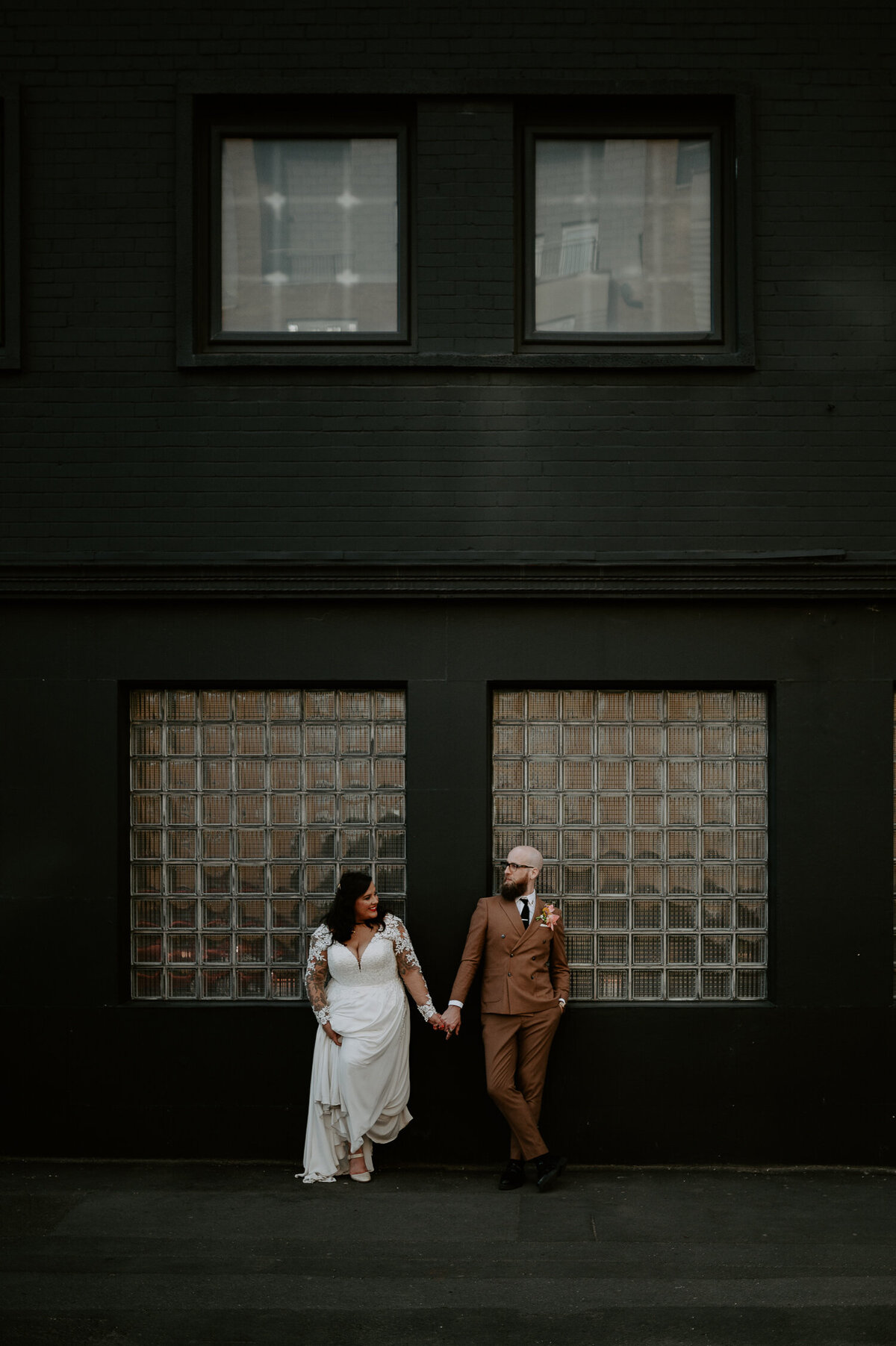 An alternative bride and groom hold hands outside their wedding venue at Five Four Studios. The black city wedding venue is a great contest on their outfits.
