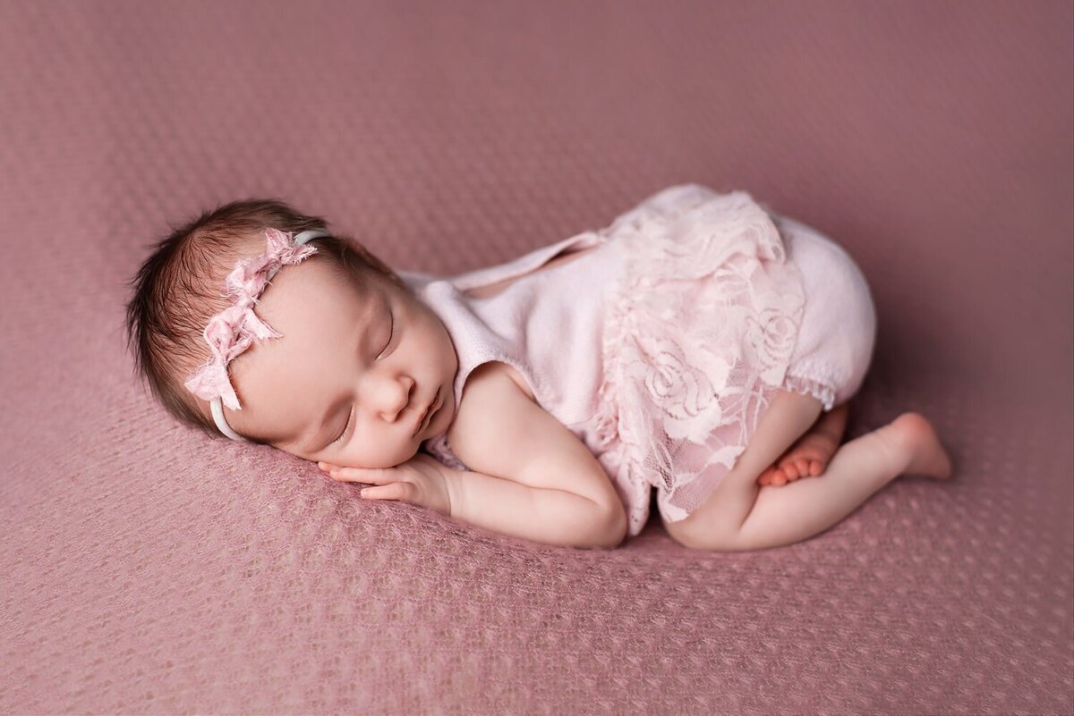 Newborn girl in pink romper in bum-up pose on a blanket.