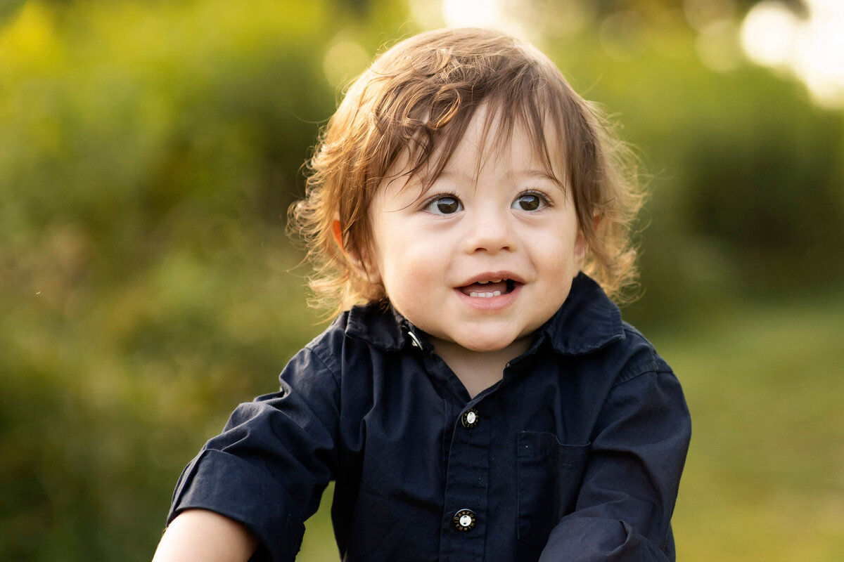 1 year old boy smiling with grassy background.