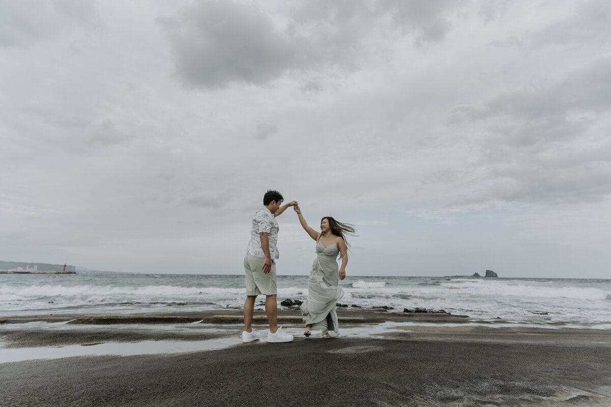 the couple holding hands and slow dancing in a beach in jeju island