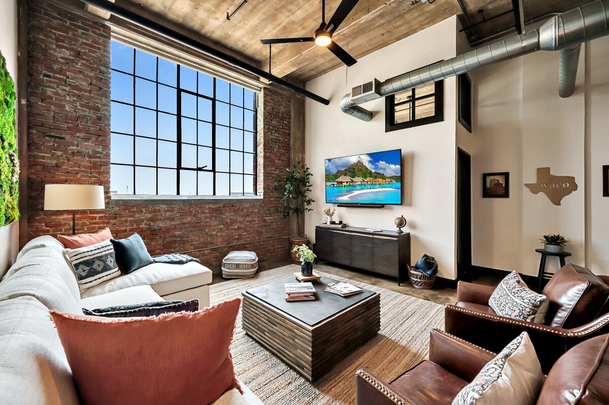 Living room with exposed brick and natural light in this 3-bedroom, 2-bathroom luxury condo in downtown Waco, TX