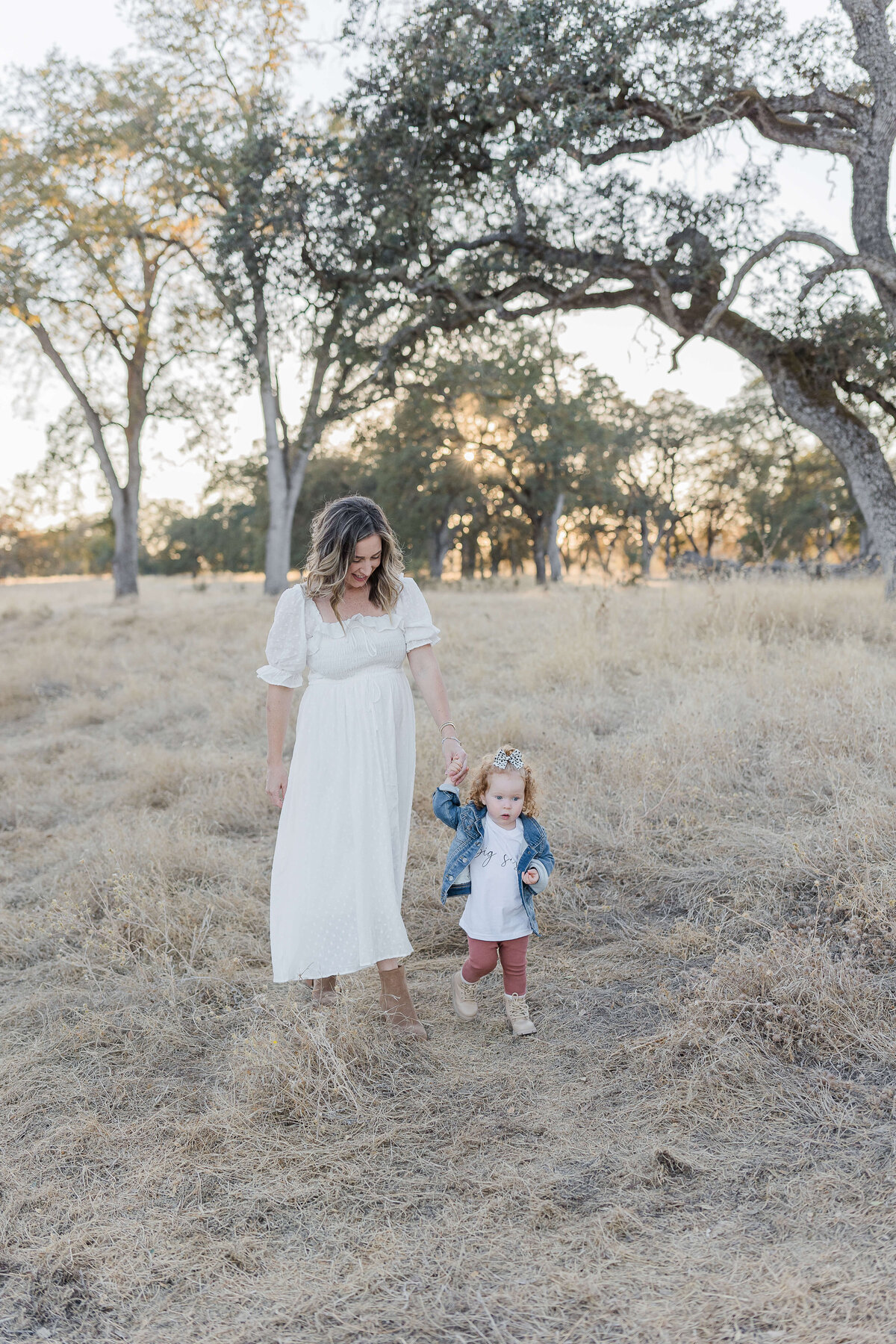 pregnant mom walking while holding her toddler daughters hand during folsom maternity photos