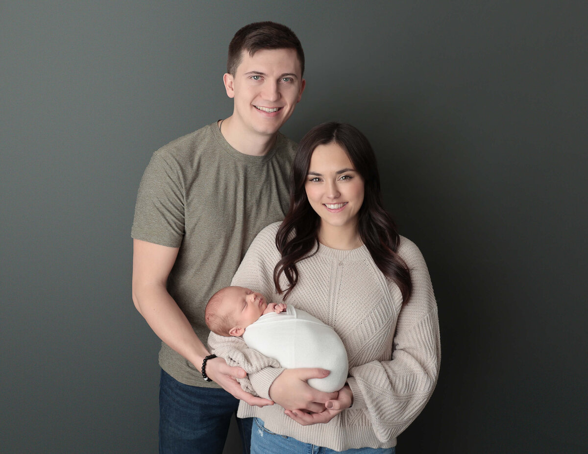 Heartwarming family portrait with a newborn girl cradled in her parents' arms, taken in a serene Rochester, NY photography studio.