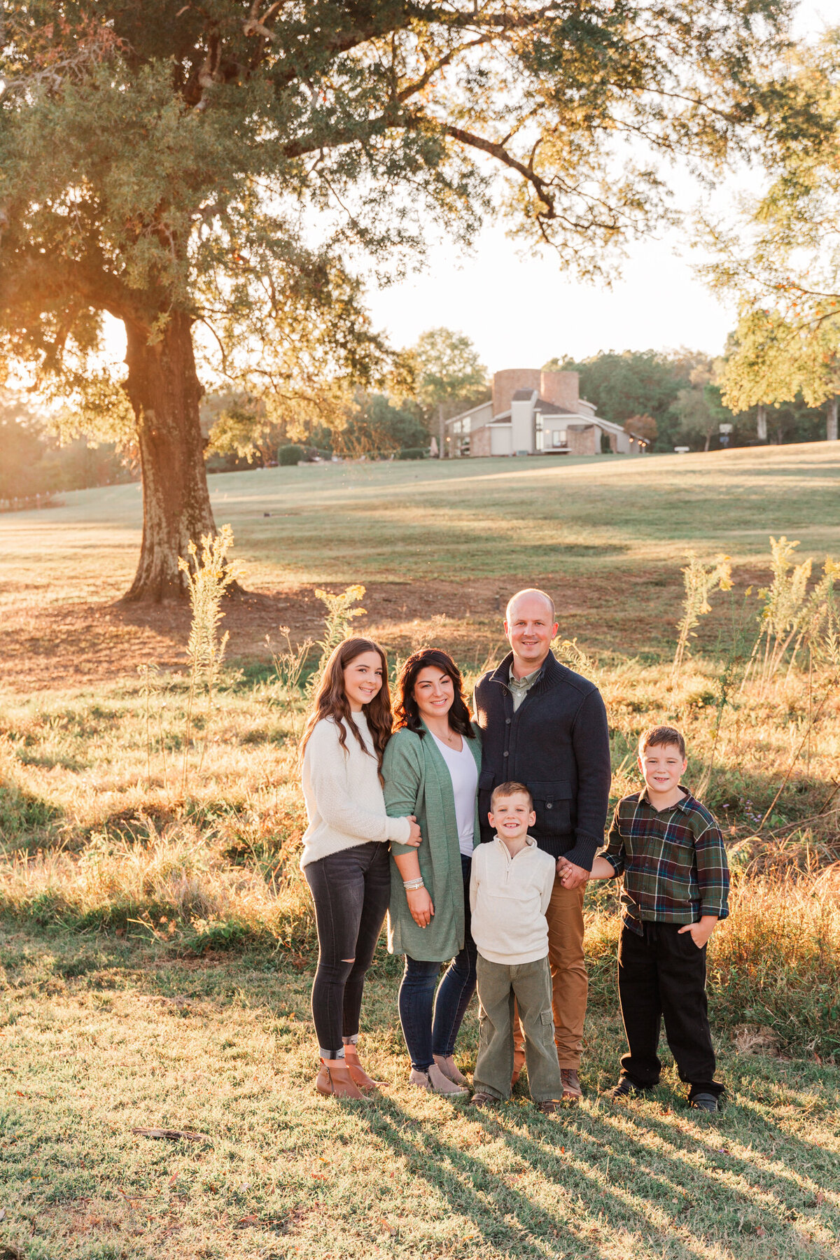 family in a field as the sun set with a tree and home in the background