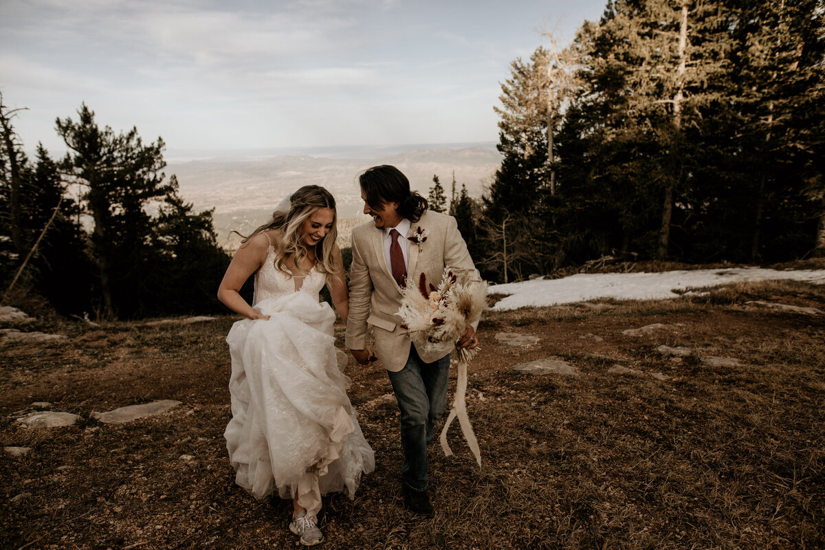 bride and groom running together on Sandia Mountains in New Mexico