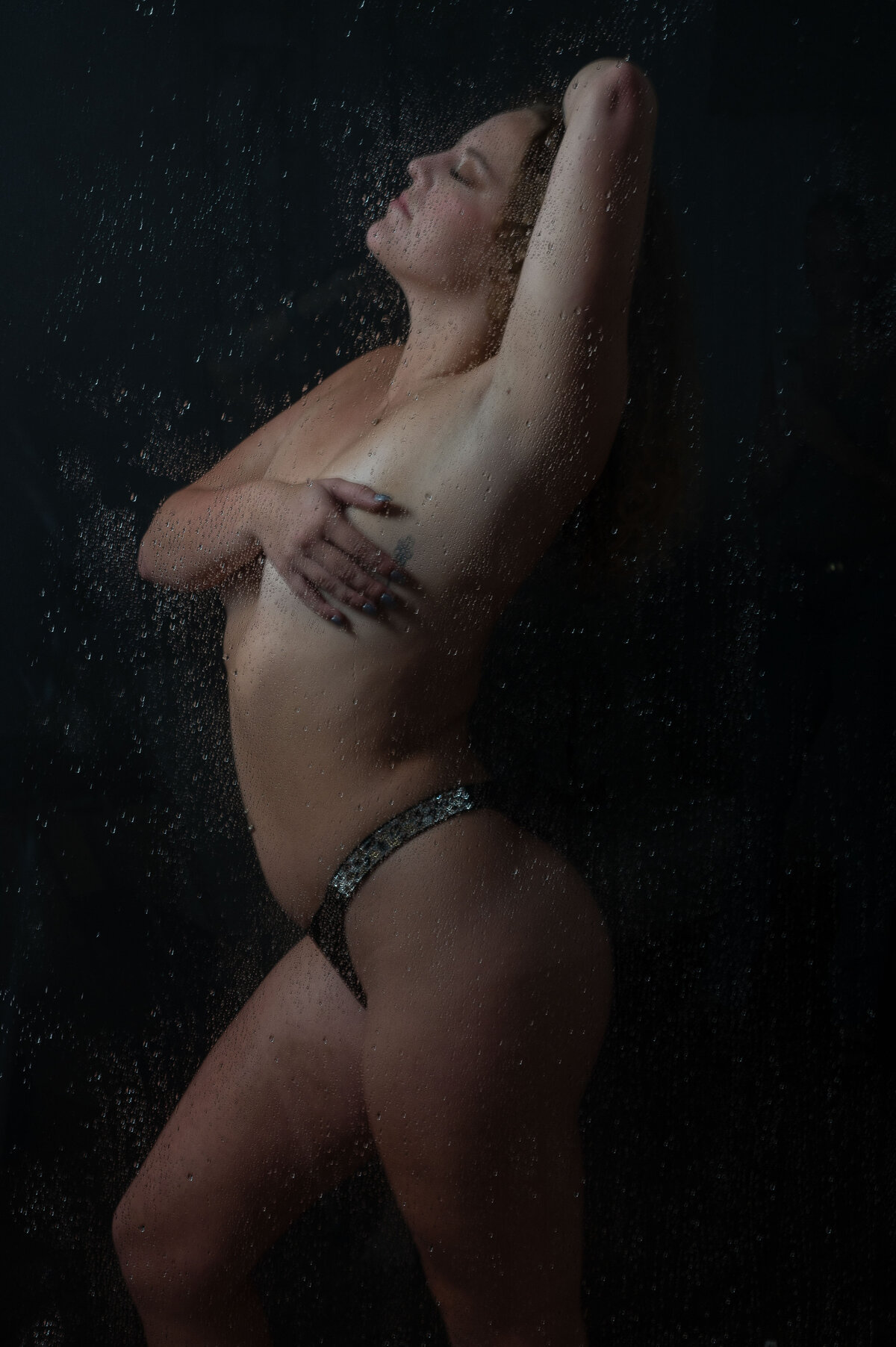 Woman posing in a shower  with one hand covering her breasts.