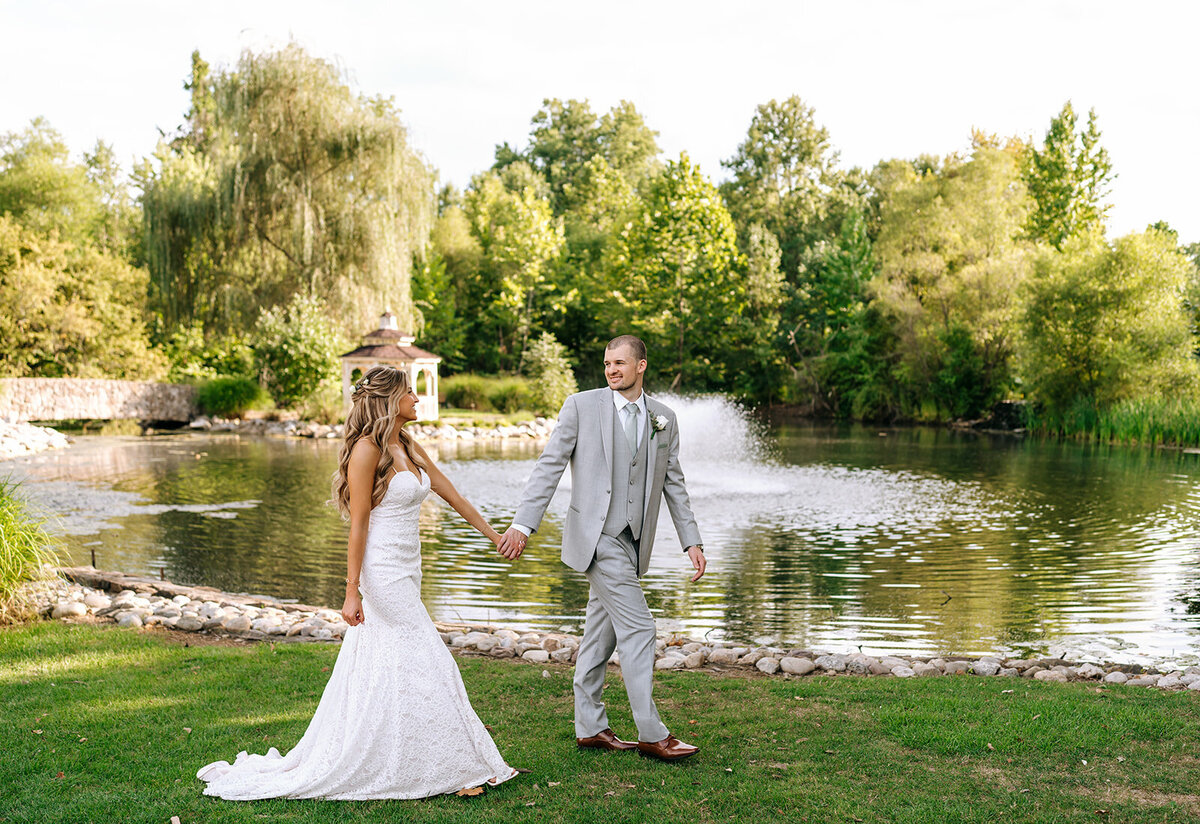 couple walking hand in hand by pond smiling