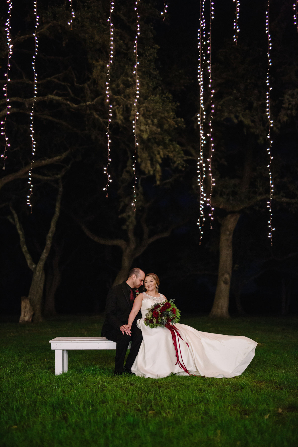 bride and groom sitting under hanging light at The Oaks at Boerne wedding venue