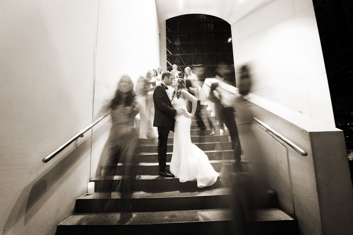 A wedding couple on a staircase with blurred figures around them.