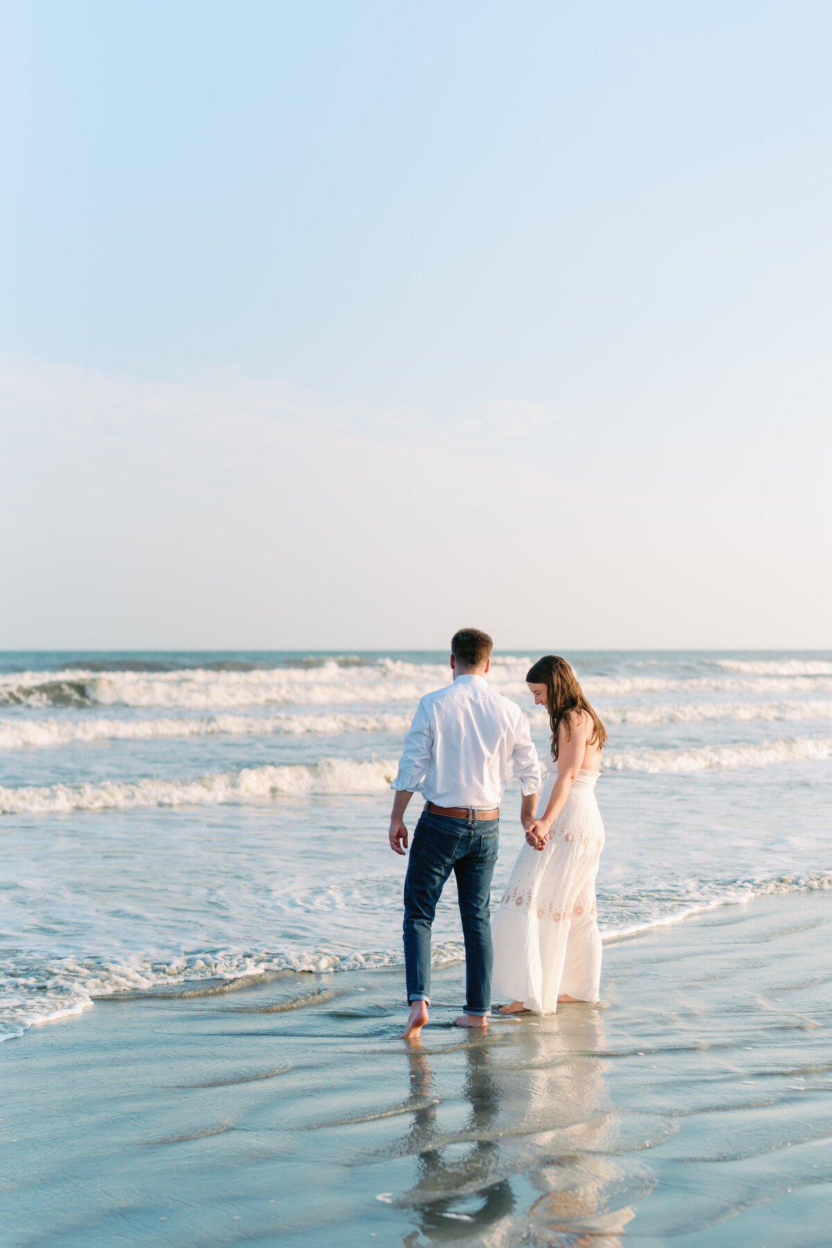 Couple lets the ocean hit their feet during sunset engagement session on Kiawah Island Beach.