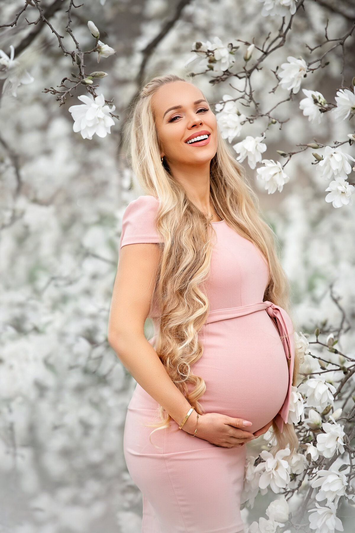 Ieva with long blond Rapunzel hair enjoying last moths of her pregnancy outside in the spring, surrounded by white tree flowers.
