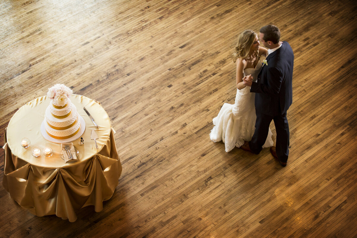 A photo of a bride and groom dancing next to their cake captured from above.
