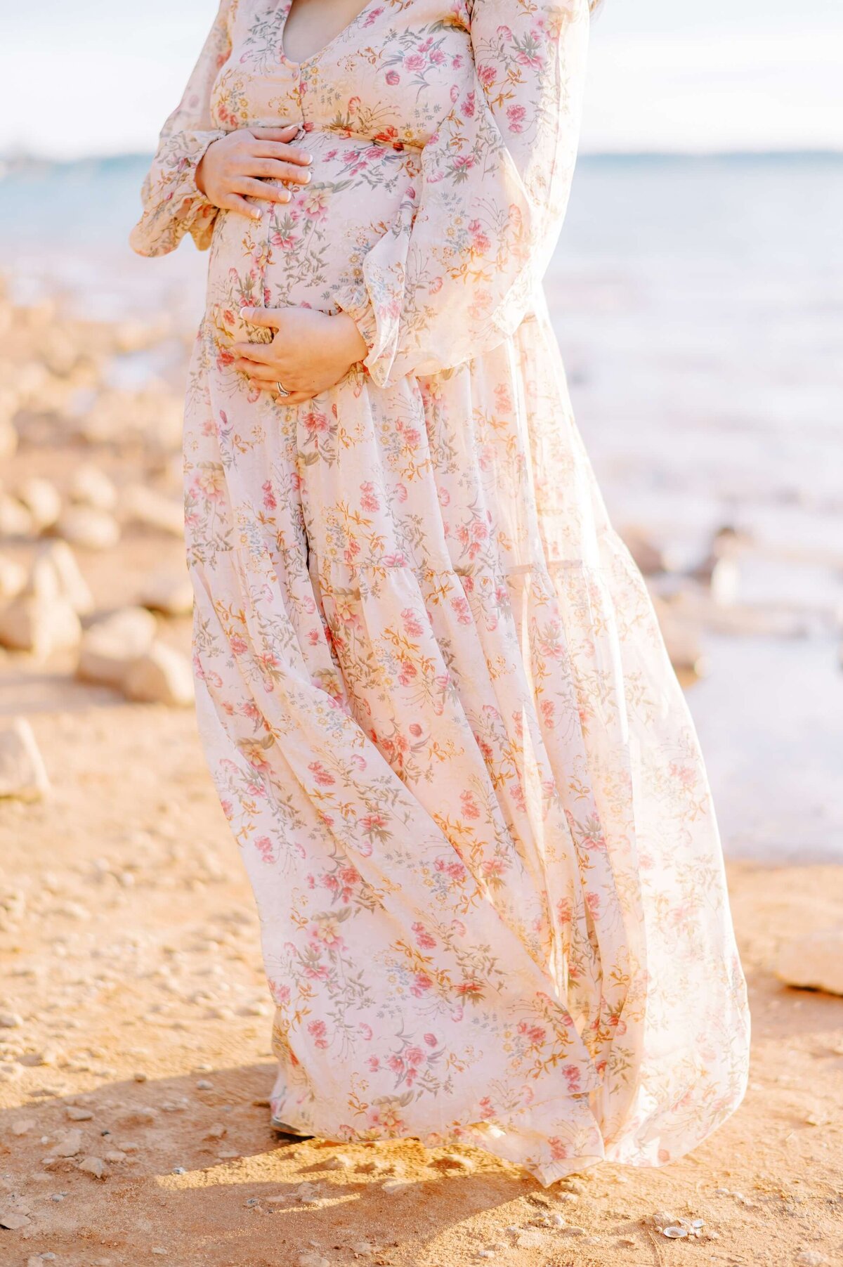 A baby jump is sweetly displayed in a pink floral dress blowing in the wind on a beach.