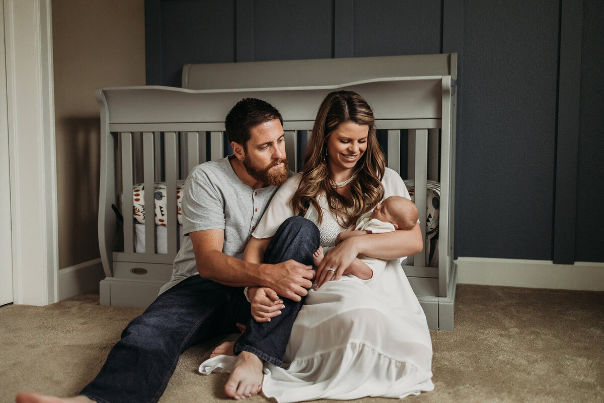 dad and mom hold baby in front of crib in neutral  nursery