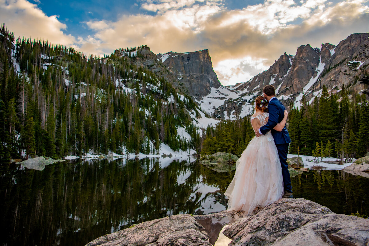 A bride and a groom kiss on top of a mountain that overlooks Rocky Mountain National Park during their Colorado Elopement. .